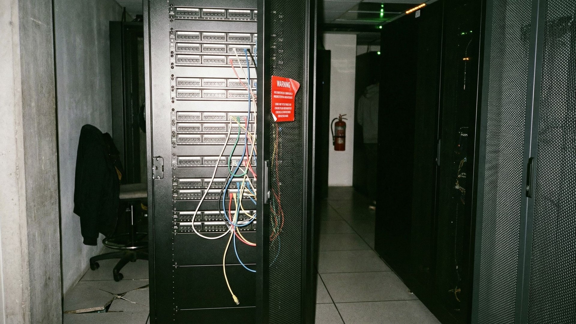 Serverrack in einem Colocation-Korridor mit losen Ethernet-Kabeln und Warn-Aufklebern, aufgenommen mit Blitzlicht