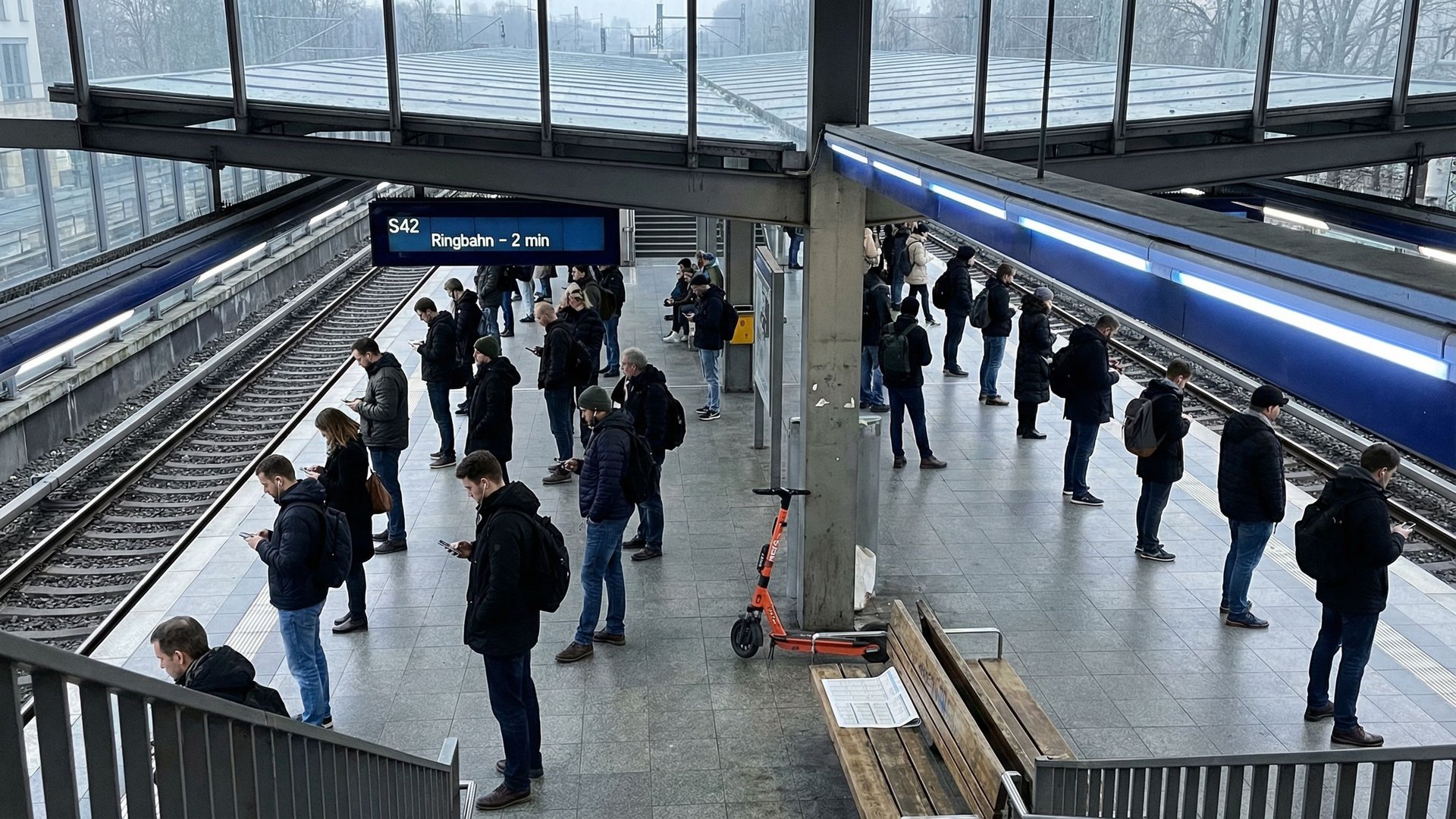 S-Bahn-Bahnsteig von oben: Dutzende Pendler stehen einzeln auf dem Bahnsteig und schauen auf ihre Smartphones, dokumentarfotografisch festgehalten als Bild kollektiver KI-Nutzung und individueller Aufmerksamkeit