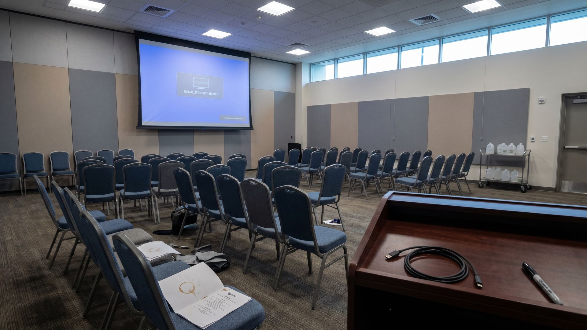 Empty conference breakout room after the final keynote session at Google Cloud Next '26 - printed agenda on a chair, projection screen dimming down